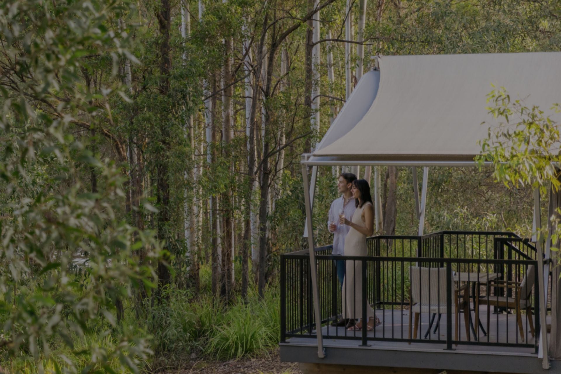 Luxury pavilion in bushland setting with couple standing on deck with a glass of wine