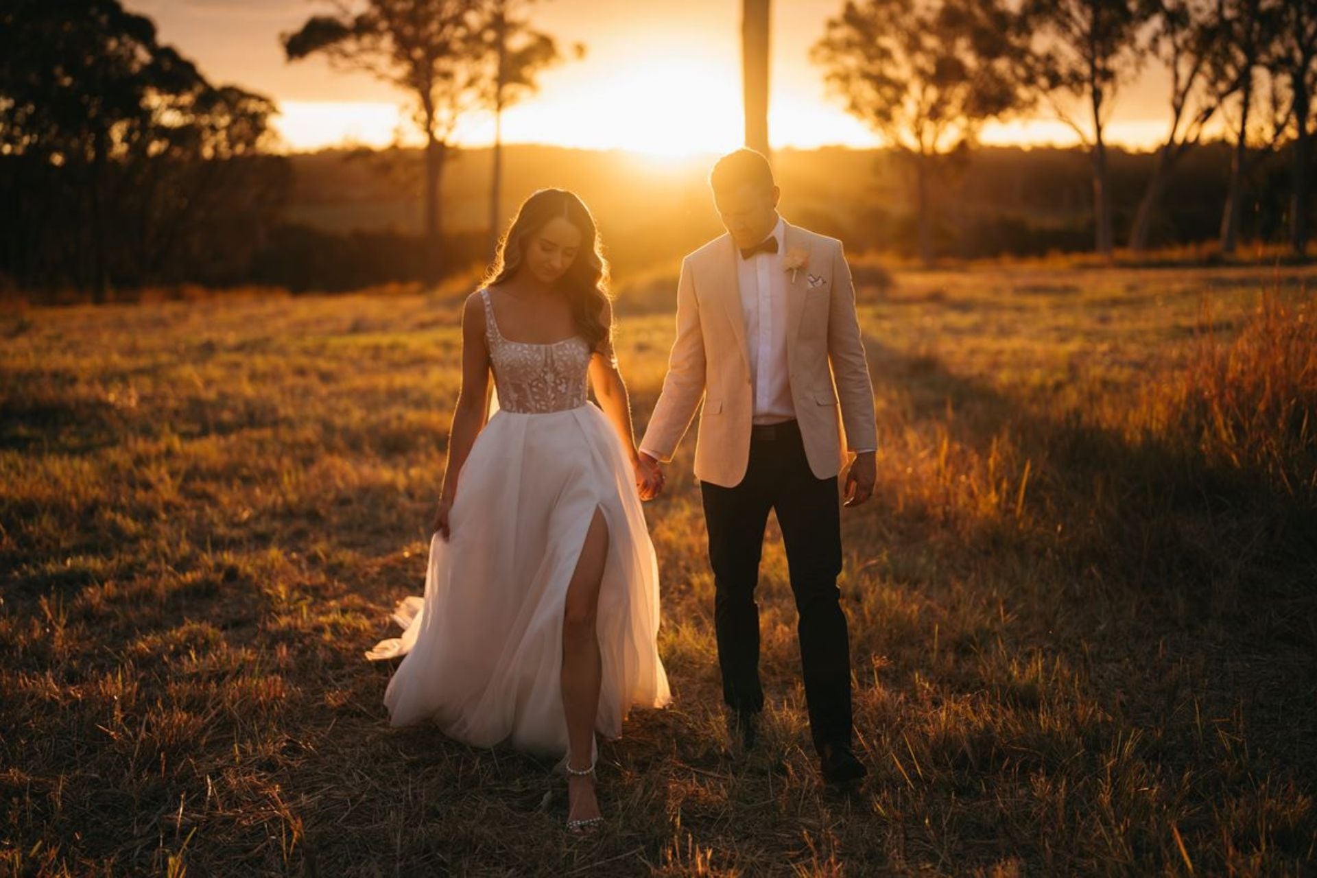 Bride and groom walking on the grassy field with a beautiful sunset in the background