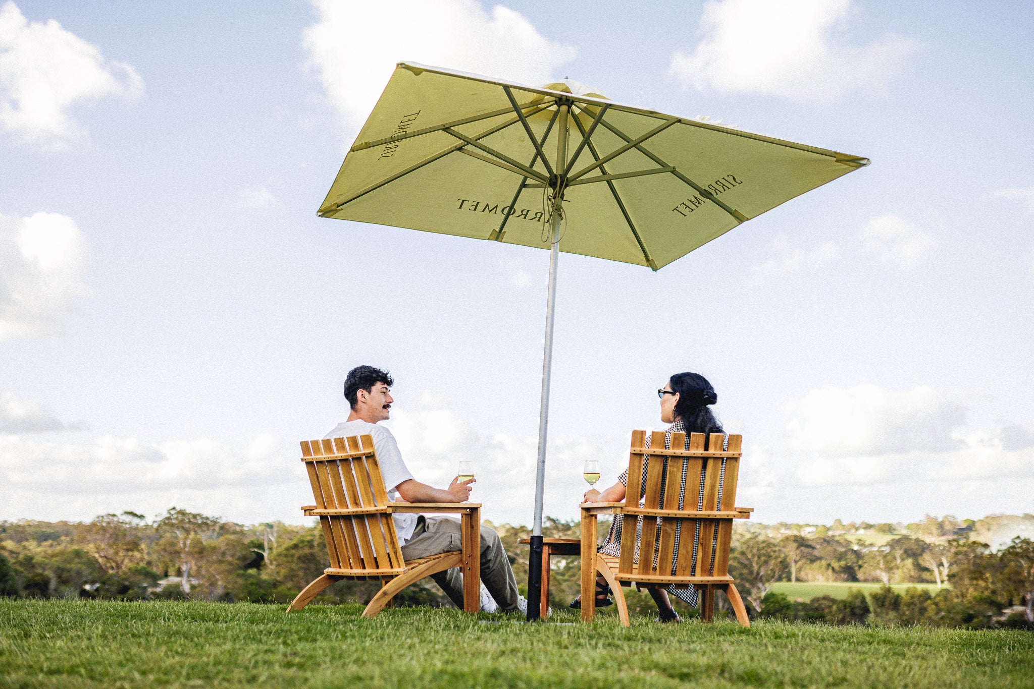 A couple enjoying a wine under an umbrella on Sirromet lawn