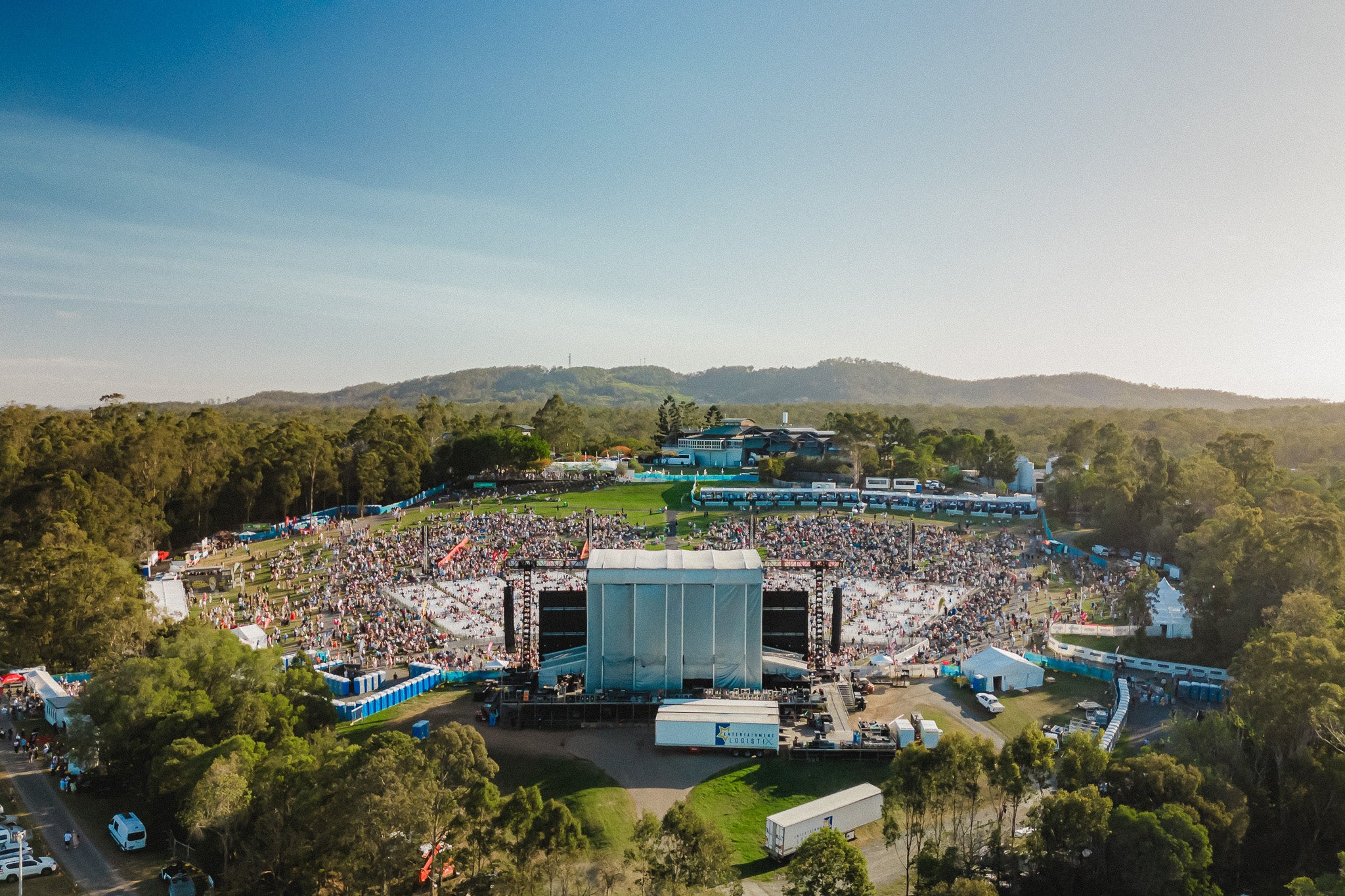 Large outdoor concert venue with stage and audience surrounded by trees