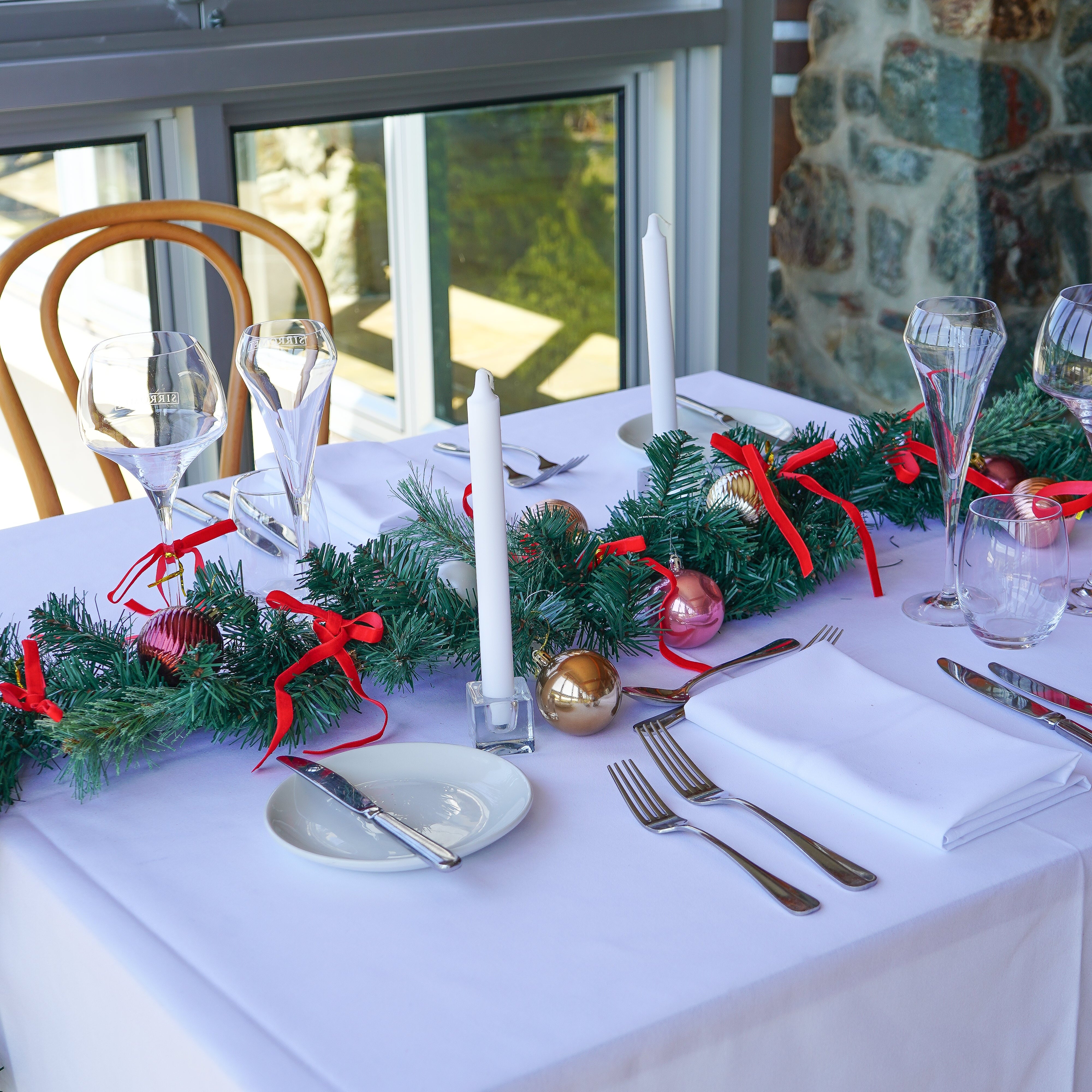 Decorated Christmas table with greenery, ornaments, and white tablecloth.