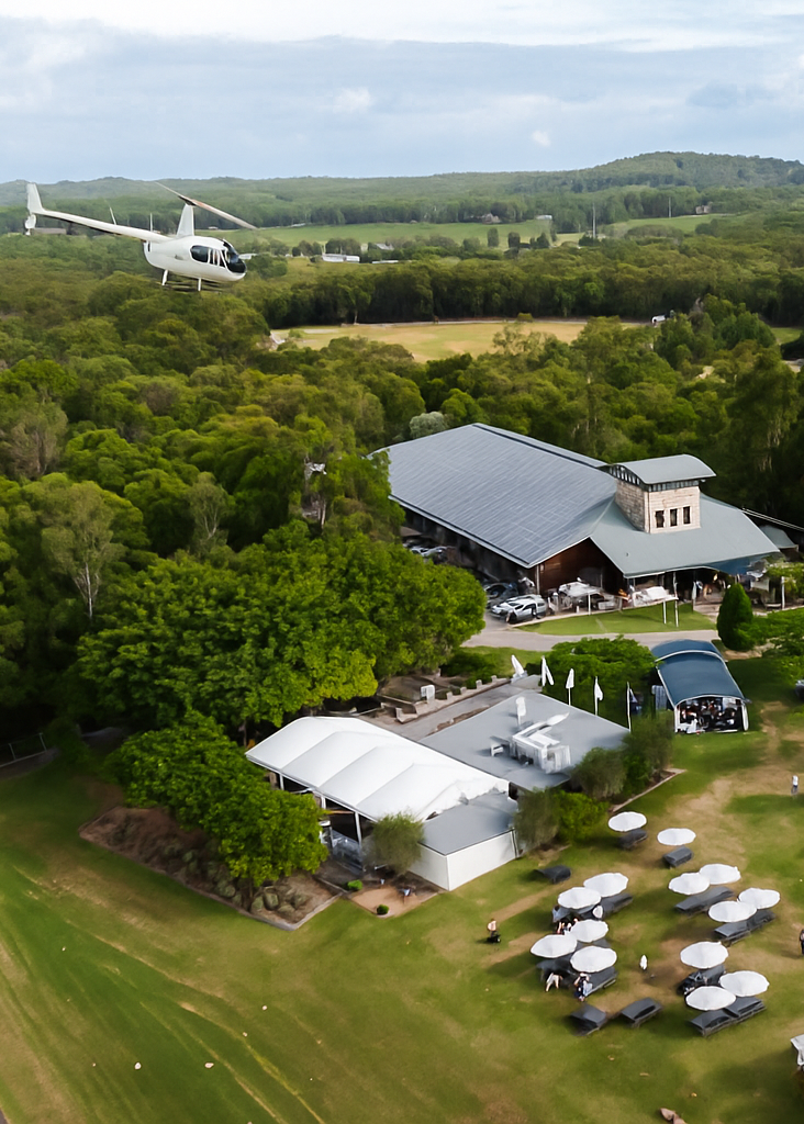 Aerial view of a building complex with outdoor seating area and helicopter in the sky.