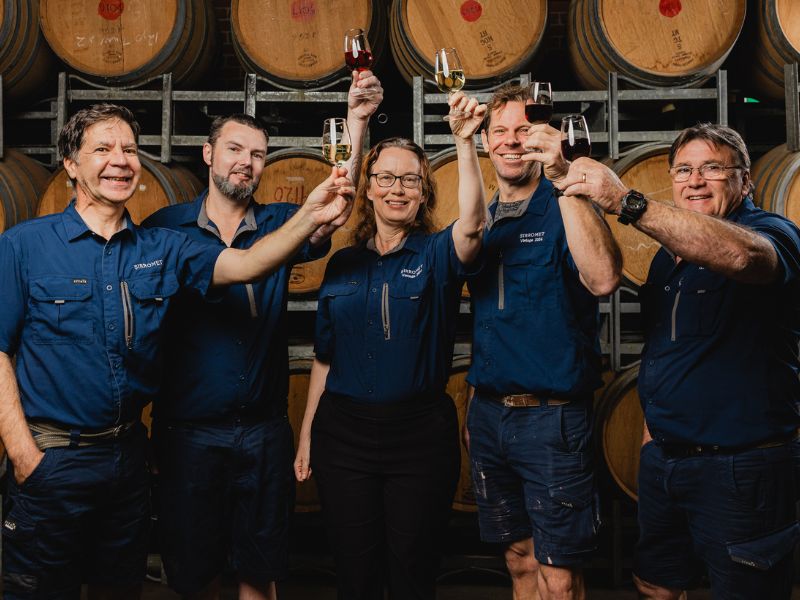 Production team standing in front of wine barrels and cheers