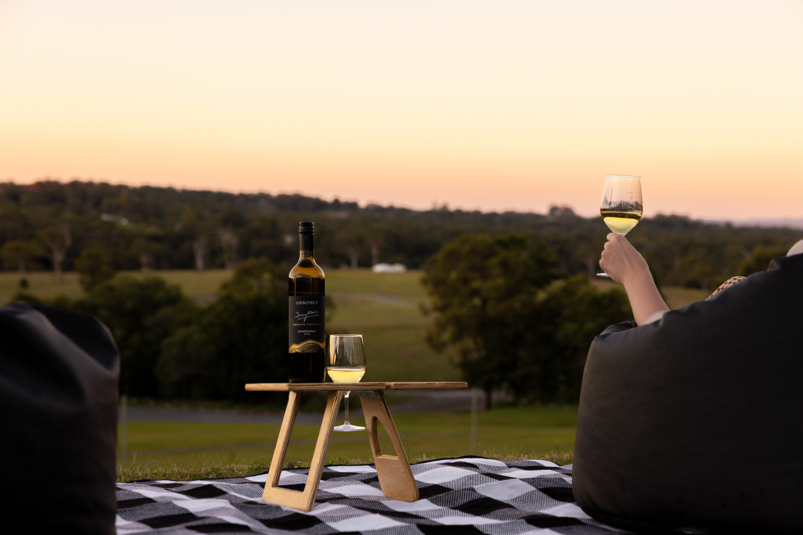 Woman sitting in bean bag holding glass of wine watching the sun go down on the lawn at Sirromet