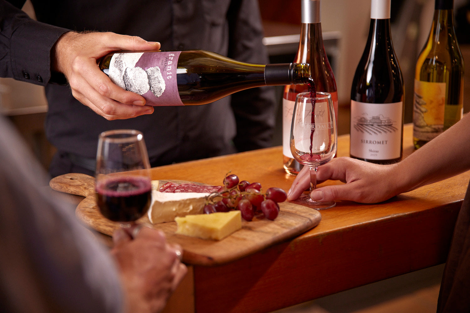 Glass of wine being poured next to a cheese platter