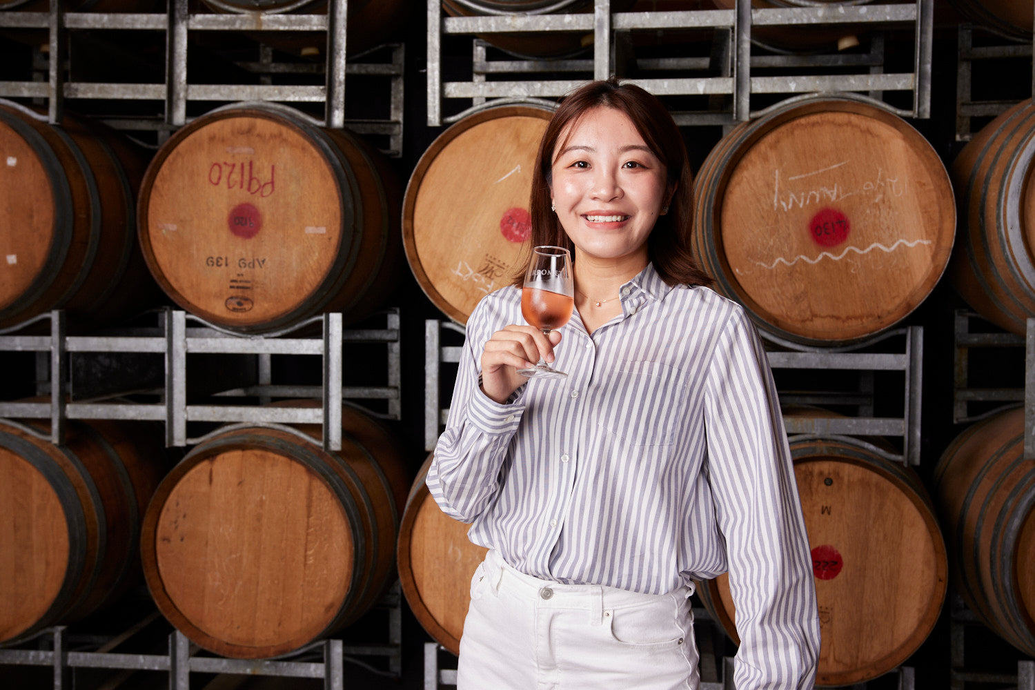 Woman holding a glass of wine in front of wooden barrels in a wine cellar