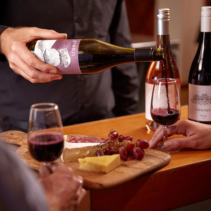 Wine being poured into a glass next to a cheese platter