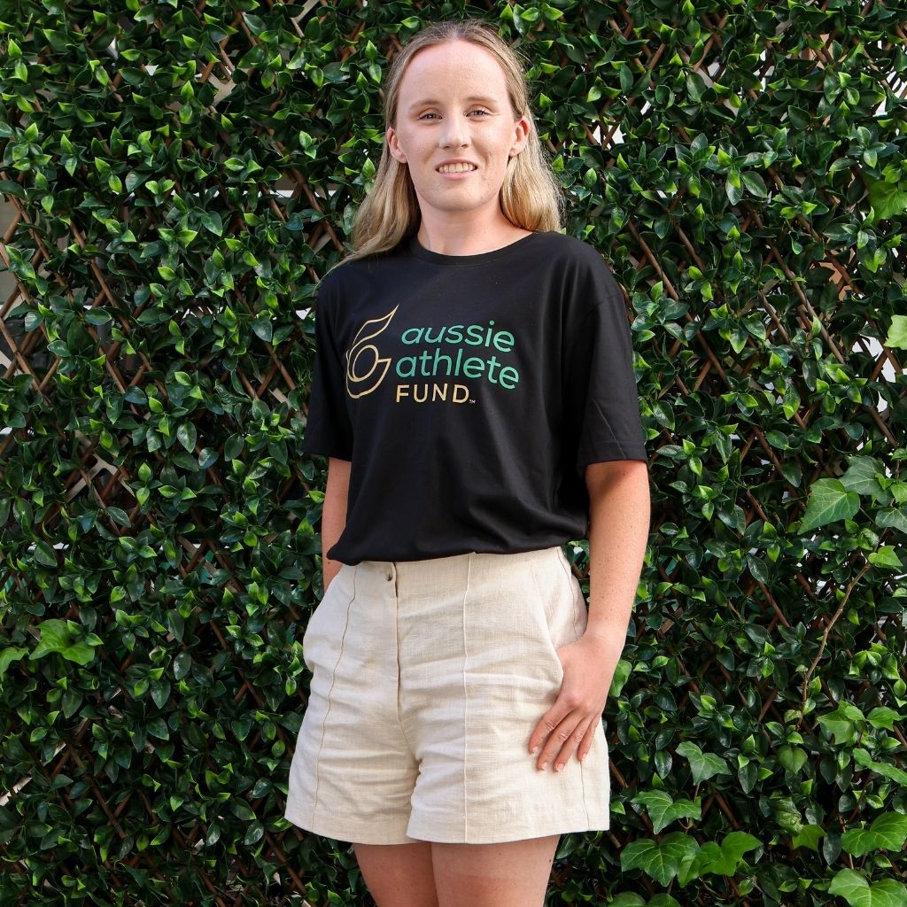 Ashley Bryden wearing a black t-shirt with 'aussie athlete fund' text standing against a green leafy background
