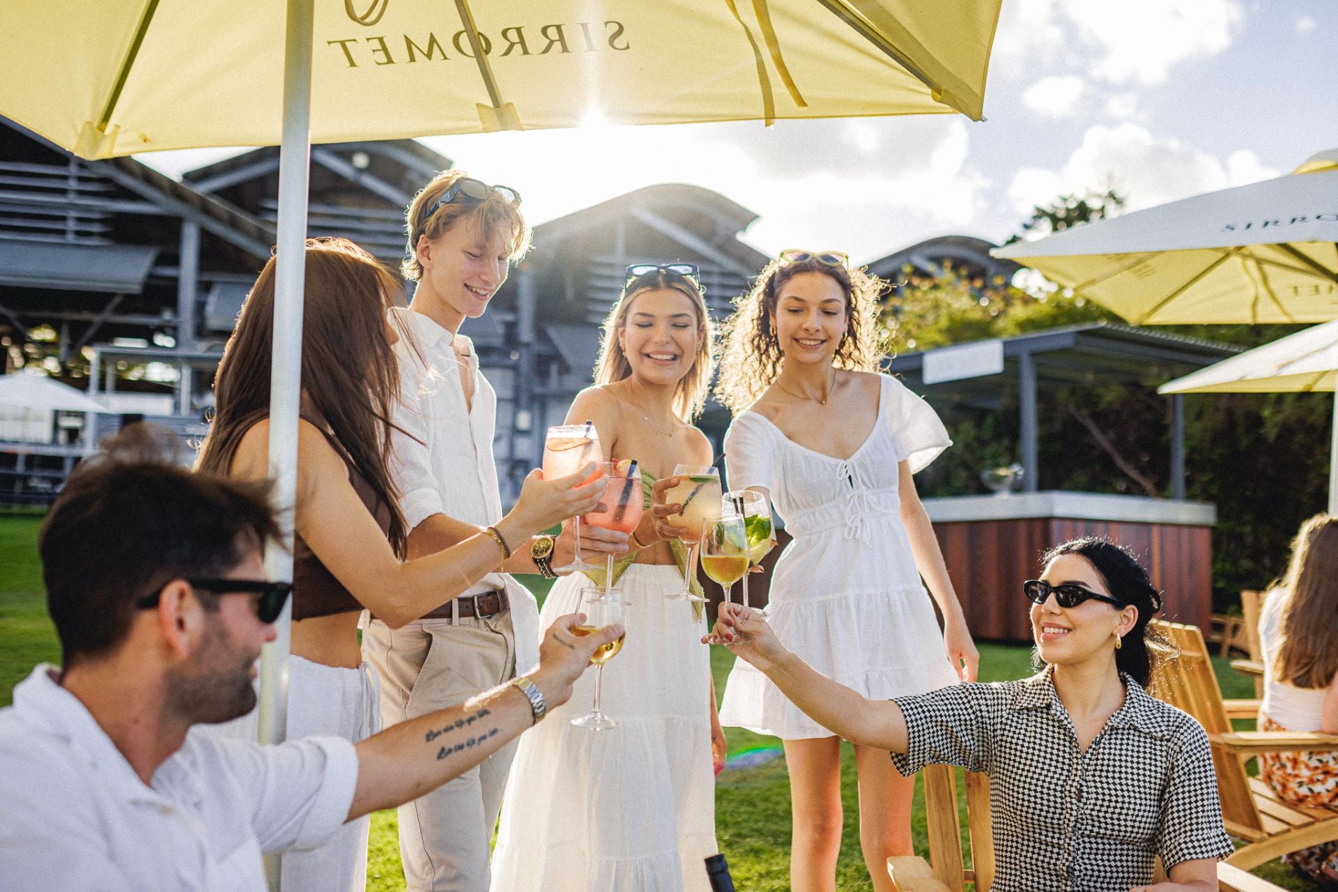 Group of friends under an umbrella on the lawn at Sirromet
