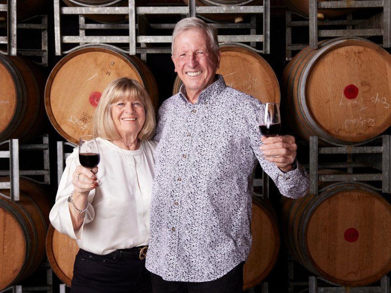 Lurleen and Terry Morris in front of wine barrels and holding wine glass each
