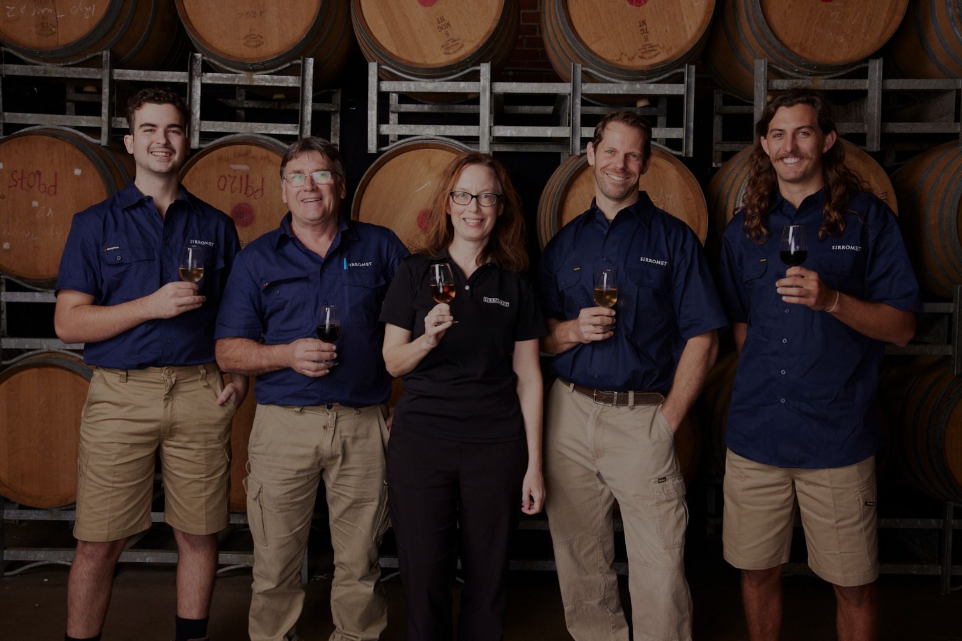 Sirromet winemakers holding a glass of wine in front of wine barrels