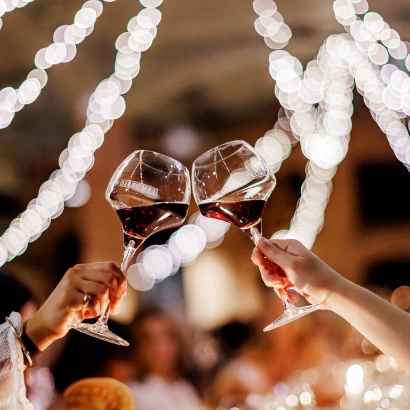 two wine glasses being "cheered" with blurred social group in the background