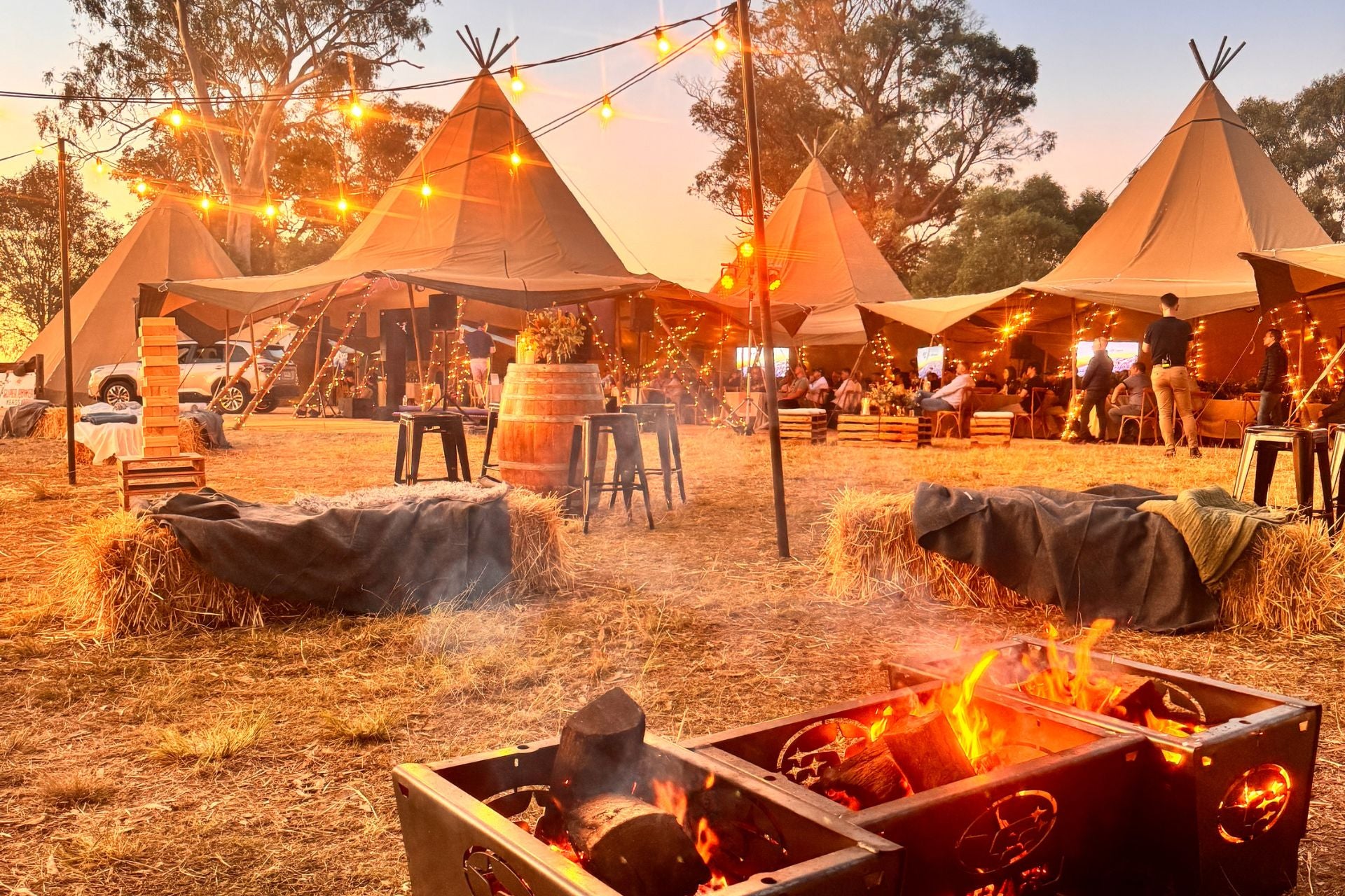Outdoor setting with tipi tents and fire pits during sunset.