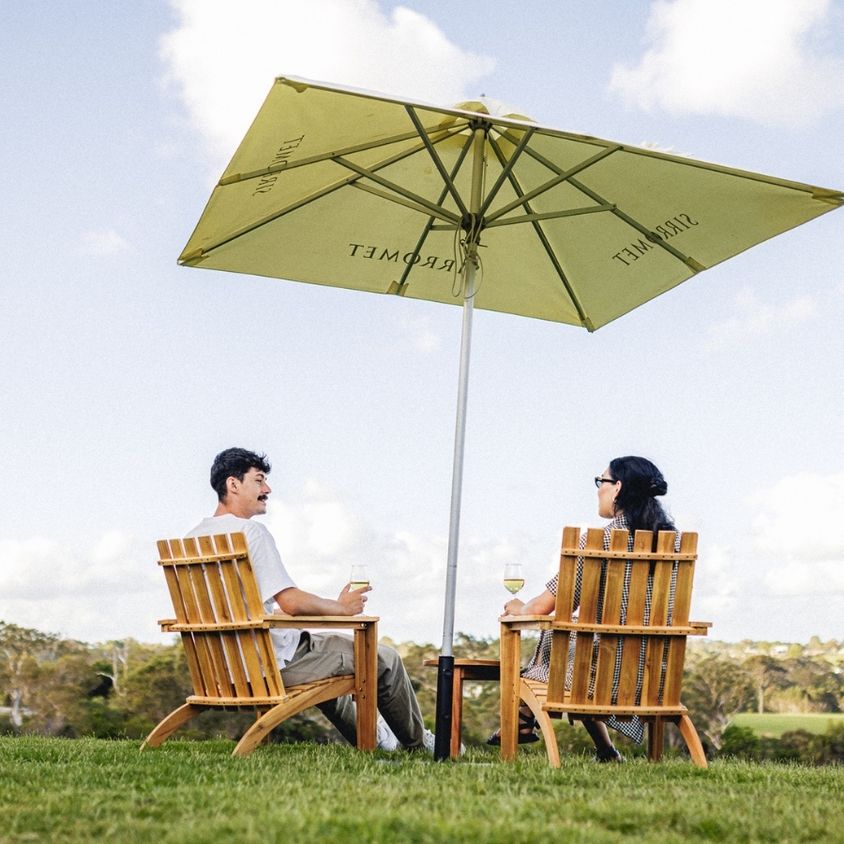 A couple enjoying a wine under an umbrella on Sirromet lawn