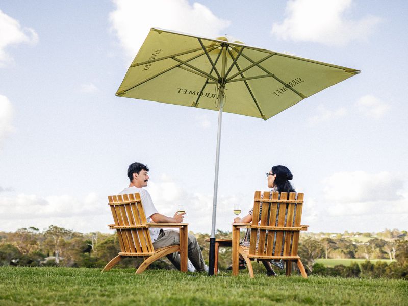 A couple enjoying a wine under an umbrella on Sirromet lawn