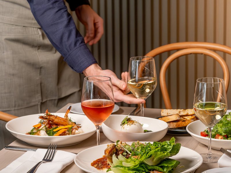 Waiter serving wine and food at dining table