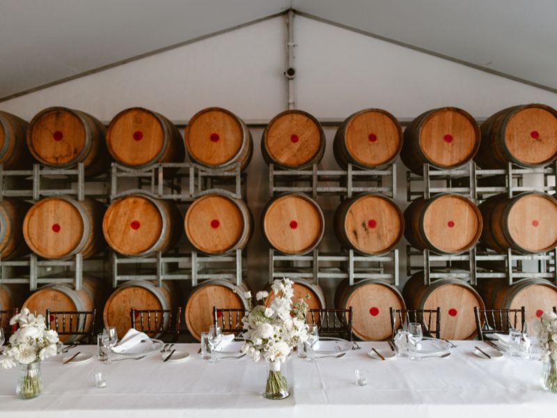 dining table set up for a wedding with rows of wine barrels in the background